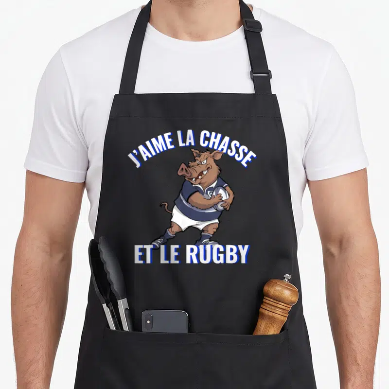 Tablier de cuisine noir avec un sanglier en maillot de rugby tenant un ballon et les mots J'aime la chasse et le rugby.