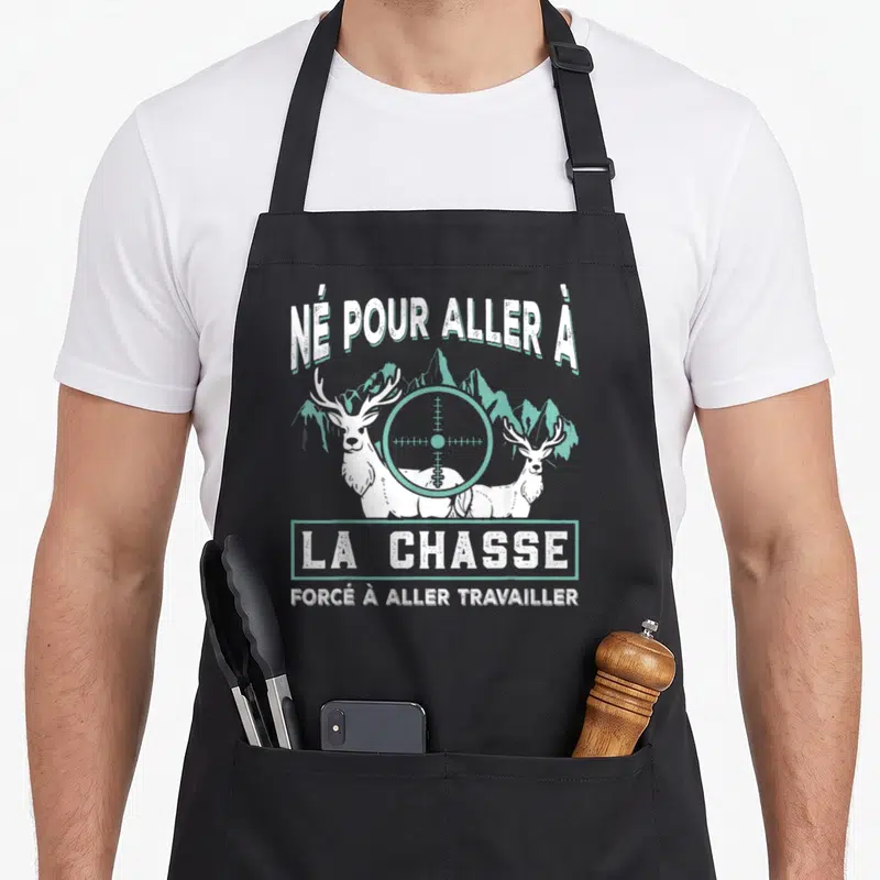 Tablier de cuisine noir avec illustration de deux cerfs blancs et un viseur de fusil sur fond de montagnes turquoise.