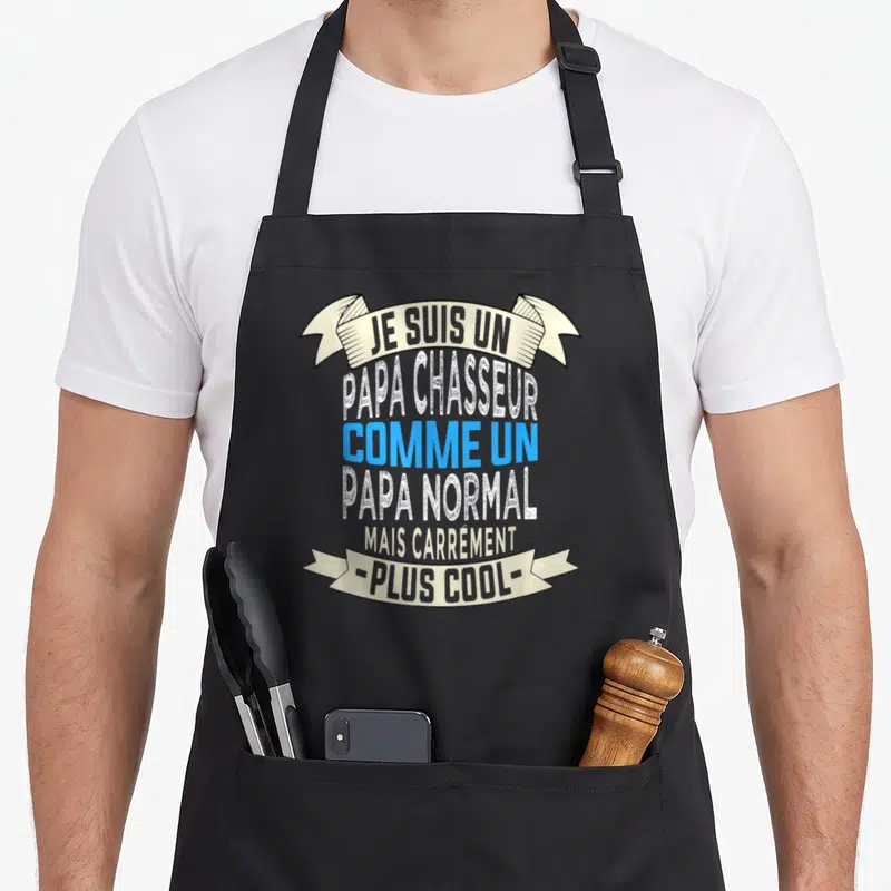 Tablier de cuisine noir avec inscription Je suis un papa chasseur comme un papa normal mais carrément plus cool sur fond de banderoles beige et texte bleu.