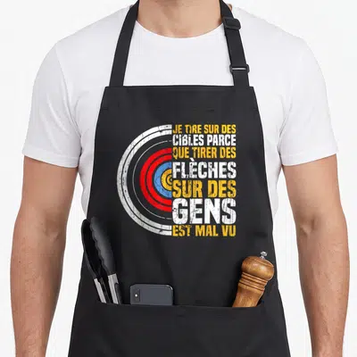 Tablier de cuisine noir avec une cible colorée et un texte humoristique en blanc et orange sur fond uni.