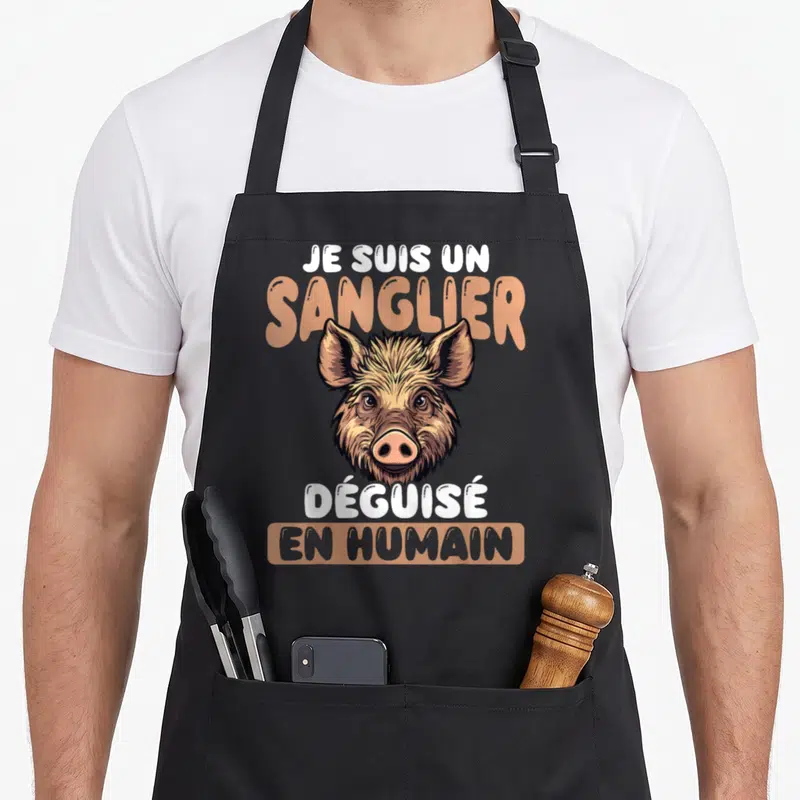 Tablier de cuisine noir avec illustration d'un visage de sanglier et texte humoristique en blanc et orange.