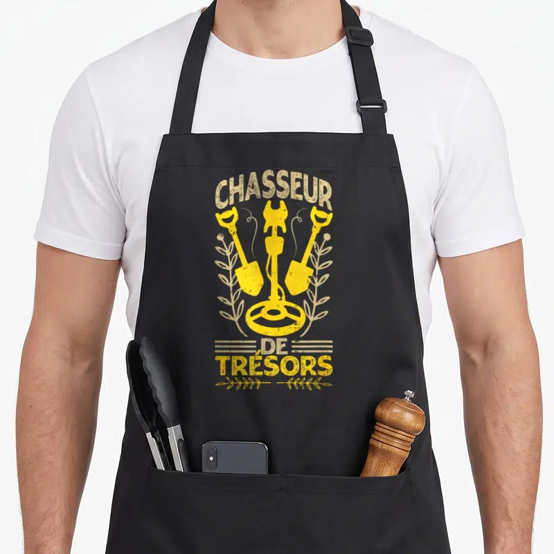 Tablier de cuisine noir avec détecteur de métal, deux bêches et le texte Chasseur de Trésors en jaune doré.