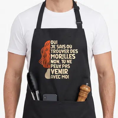 Tablier de cuisine noir avec profil femme orange et texte beige sur la chasse aux morilles.