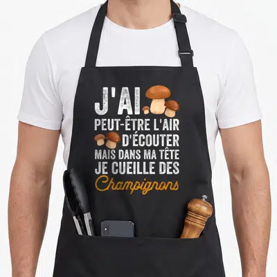 Tablier de cuisine noir avec texte blanc et orange illustré de trois cèpes colorés sur fond uni.