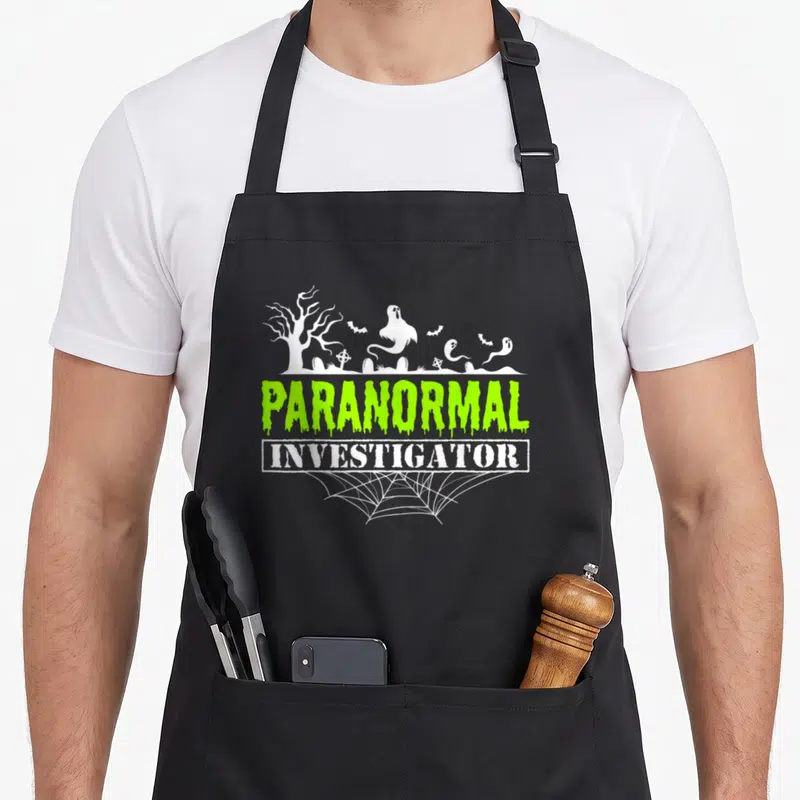 Tablier de cuisine noir avec motif Enquêteur paranormal et illustrations de fantômes blancs sur fond gris.
