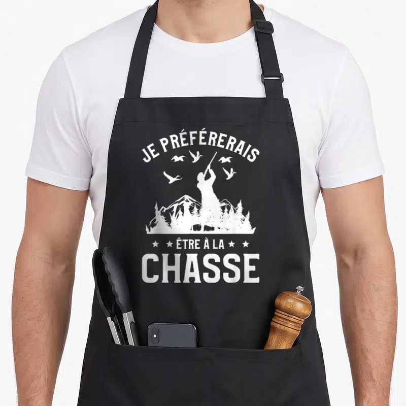 Tablier de cuisine noir avec une silhouette blanche de chasseur tirant vers des oiseaux en vol devant un paysage de montagnes et d'arbres.