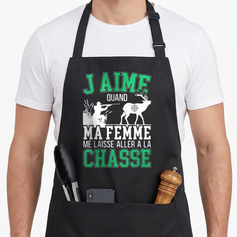 Tablier de cuisine noir avec inscription verte et blanche J'aime quand ma femme me laisse aller à la chasse sur fond gris uni.