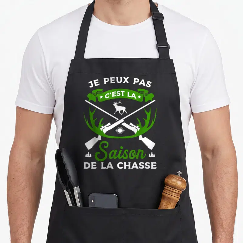 Tablier de cuisine noir avec deux fusils croisés, un cerf et une banderole verte portant le texte Je peux pas c'est la saison de la chasse.