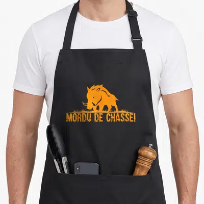 Tablier de cuisine noir avec silhouette orange de sanglier et inscription Mordu de chasse en bas du motif central.