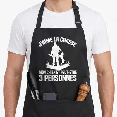 Tablier de cuisine noir avec silhouette blanche chasseur et chien sous le texte J'aime la chasse mon chien et peut-être 3 personnes.