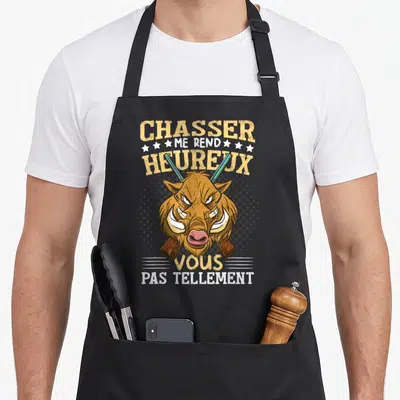 Tablier de cuisine noir avec tête de sanglier, fusils croisés et texte humoristique en jaune et blanc.