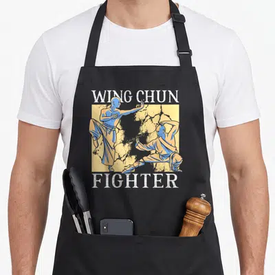 Tablier de cuisine noir avec illustration de deux pratiquants de Wing Chun et le texte WING CHUN FIGHTER en blanc.