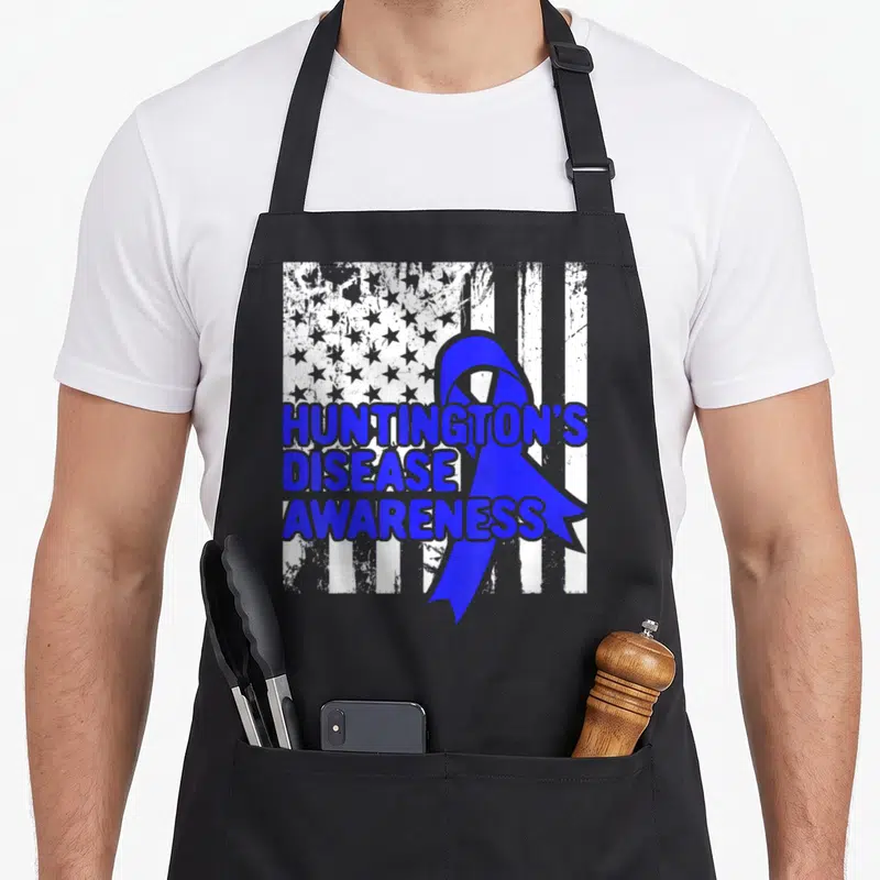 Tablier de cuisine noir avec ruban bleu et texte Huntington's Disease Awareness sur fond de drapeau américain délavé.