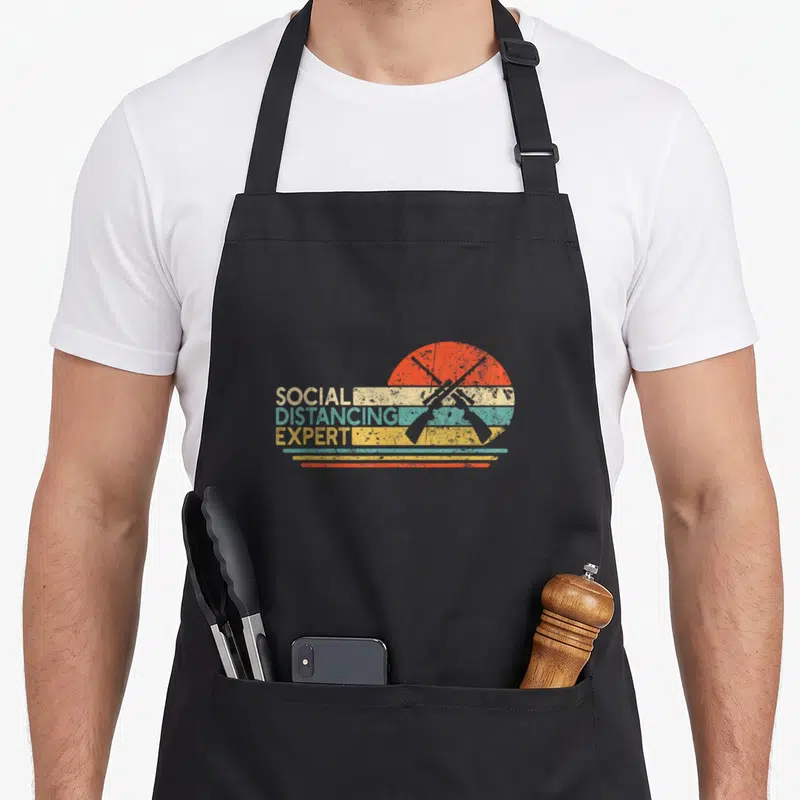 Tablier de cuisine noir avec motif Social Distancing Expert et fusils croisés sur fond coloré vintage