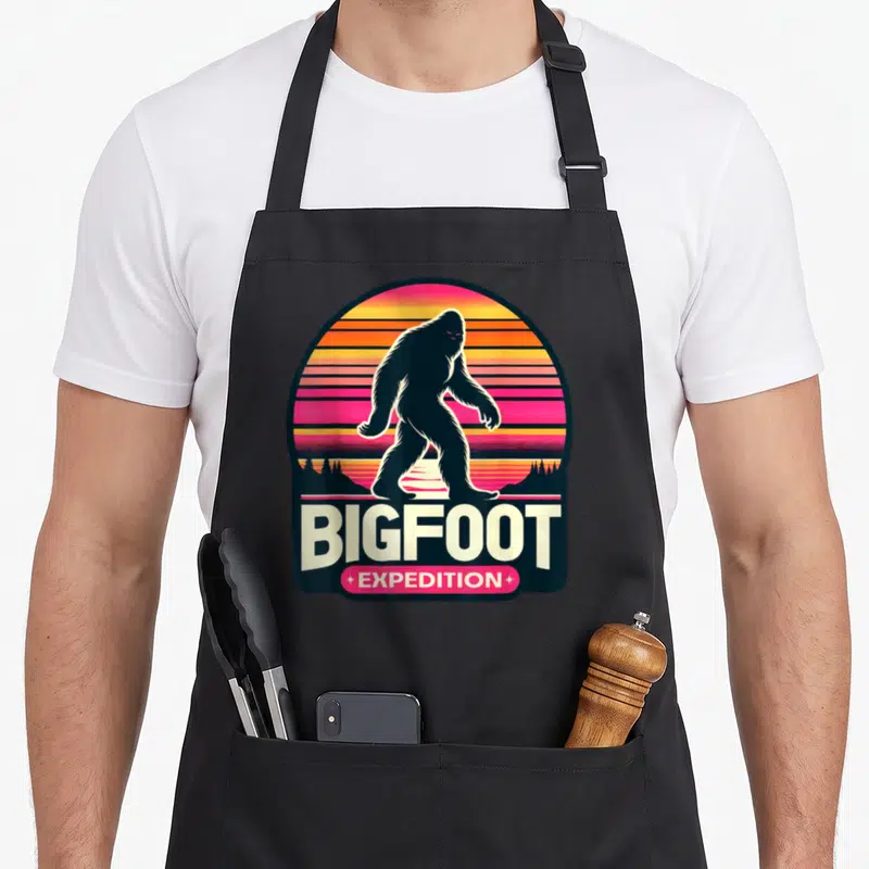 Tablier de cuisine noir avec silhouette Bigfoot et texte Bigfoot Expedition sur fond de sunset rétro.