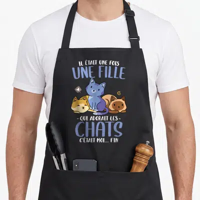 Tablier de cuisine noir avec trois chats colorés et le texte Il était une fois une fille qui adorait les chats c'était moi fin imprimé en bleu et blanc.