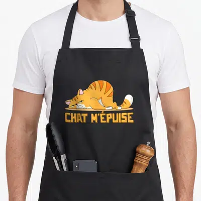 Tablier de cuisine noir avec illustration d'un chat tigré orange couché et du texte CHAT M'ÉPUISE en lettres capitales jaunes.