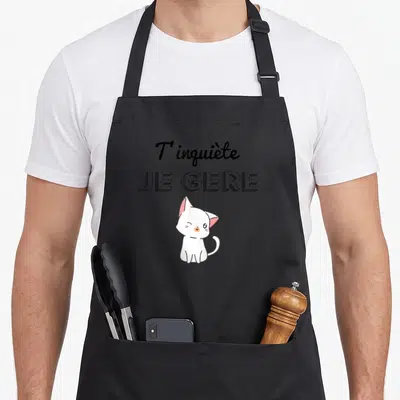 Tablier de cuisine noir avec un chat blanc kawaii et l'inscription T'inquiète Je Gère en typographie noire.