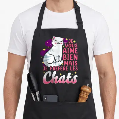 Tablier de cuisine noir avec un chat blanc rayé et le texte Je vous aime bien mais je préfère les chats en lettres roses.