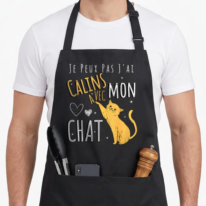Tablier de cuisine noir avec illustration d'un chat orange pointant vers le texte Je peux pas j'ai calins avec mon chat.