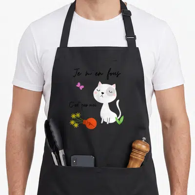 Tablier de cuisine noir avec un chat blanc assis, une ampoule brisée et les mots Je m'en fous C'est pas moi.