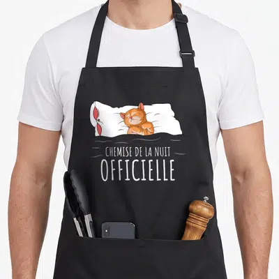 Tablier de cuisine noir avec illustration d'un chat roux dormant sur un oreiller et le texte chemise de la nuit « officielle ».