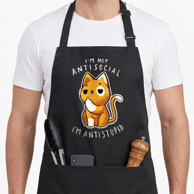Tablier de cuisine noir avec illustration d'un chat orange et blanc posant une patte sur sa bouche avec texte blanc.