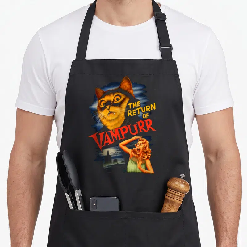 Tablier de cuisine noir avec illustration d'un chat vampire orange et une femme terrifiée sur fond bleu nuit.