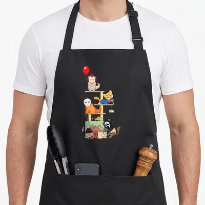 Tablier de cuisine noir avec des chats déguisés en personnages de films d'horreur sur un meuble à chat.