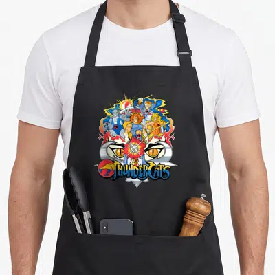 Tablier de cuisine noir avec illustration colorée de Thundercats, yeux de félin et logo stylisé au centre.
