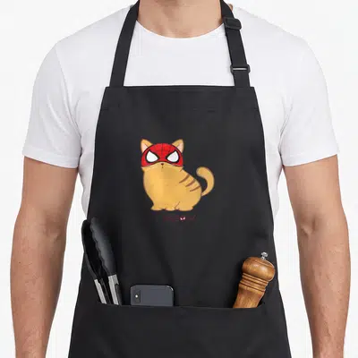 Tablier de cuisine noir avec un chat orange portant un masque rouge de super-héros et le mot meow imprimé en dessous.