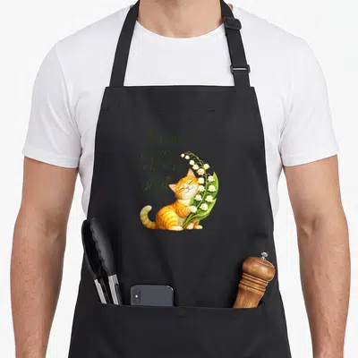 Tablier de cuisine noir avec un chat tigré tenant des muguet et une inscription manuscrite verte.