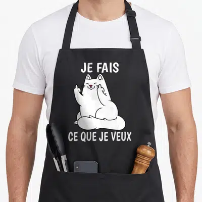 Tablier de cuisine noir avec un chat blanc dessiné levant deux doigts et le texte Je fais ce que je veux en lettres blanches.