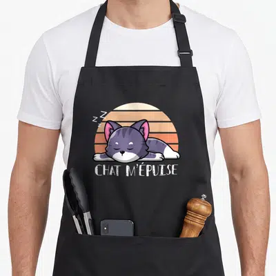 Tablier de cuisine noir avec un chaton gris dormant sur fond orange et le texte chat m'épuise en blanc.