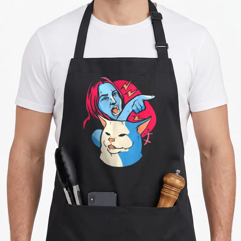 Tablier de cuisine noir avec une femme bleue pointant un chat blanc impassible sur fond rose.
