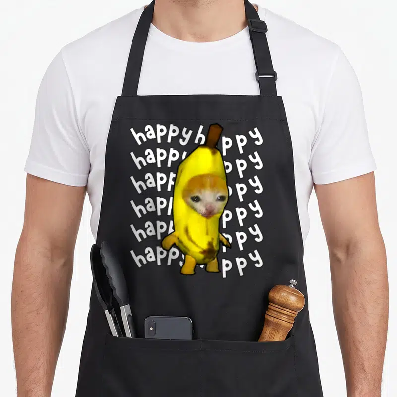Tablier de cuisine noir avec un chat orange enveloppé dans une banane jaune et des mots happy en arrière-plan blanc.