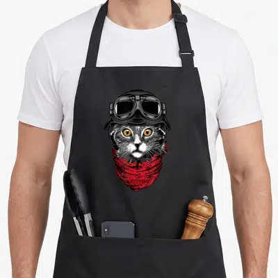 Tablier de cuisine noir avec illustration d'un chat gris portant un casque de moto et un foulard rouge orné de fleurs de lys.
