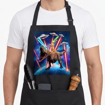 Tablier de cuisine noir avec illustration d'un chat tigré monté sur un dinosaure T-Rex sous des Ufo tirant des lasers spatiaux.