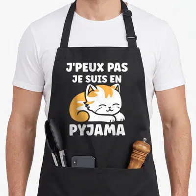 Tablier de cuisine noir avec un chat orange et blanc dormant et le texte Je peux pas je suis en pyjama en blanc.