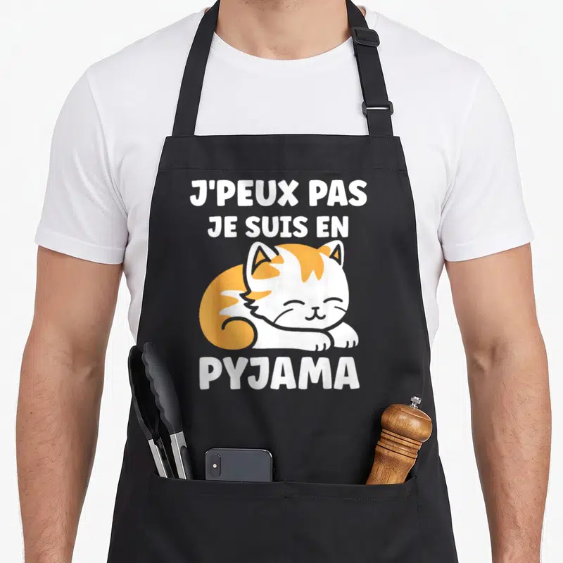 Tablier de cuisine noir avec un chat orange et blanc dormant et le texte Je peux pas je suis en pyjama en blanc.