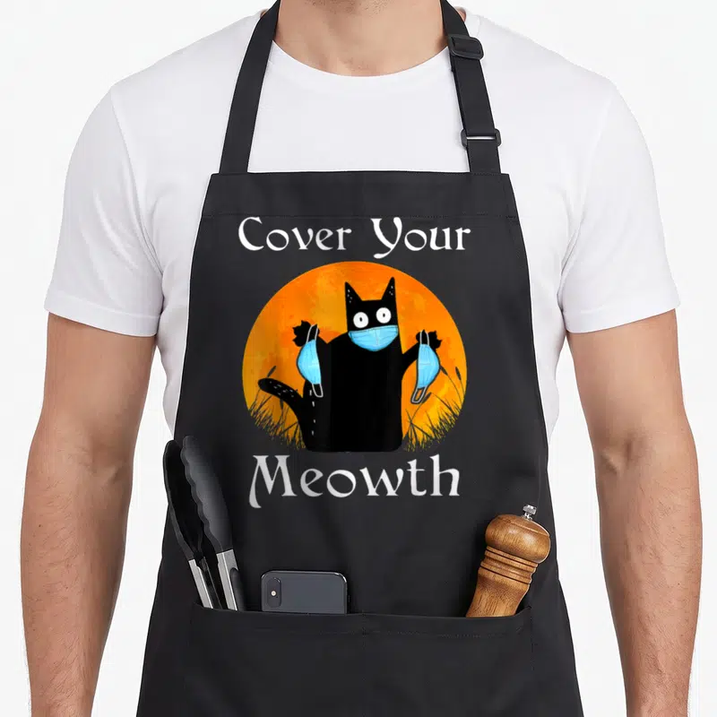 Tablier de cuisine noir avec un chat noir tenant des masques bleus devant une lune orange.