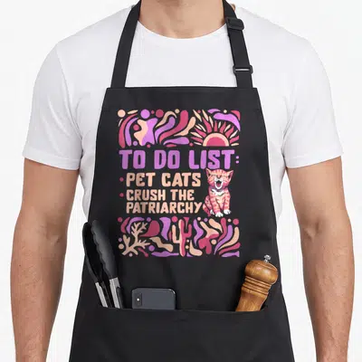 Tablier de cuisine noir avec illustration colorée d'un chat et texte anglais To Do List Pet Cats Crush The Patriarchy.
