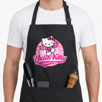 Tablier de cuisine noir avec Hello Kitty en tenue de cheerleading tenant des pompons roses sur fond circulaire rose et étoiles blanches.