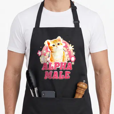 Tablier de cuisine noir avec un chaton orange entouré de fleurs et le texte Alpha Male en rose.