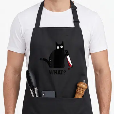 Tablier de cuisine noir avec illustration d'un chat noir tenant un couteau ensanglanté et le texte What?