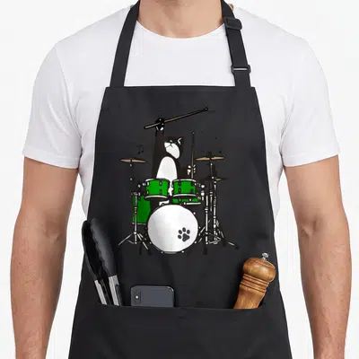 Tablier de cuisine noir avec illustration d'un chat batteur jouant d'une batterie verte et de cymbales.