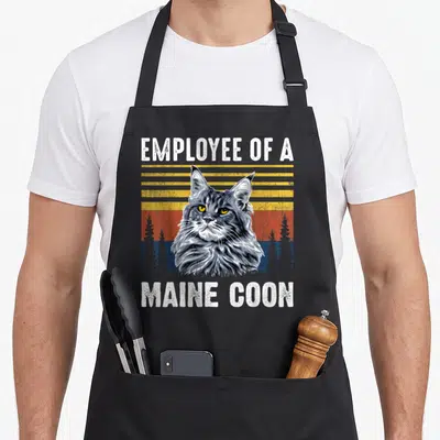 Tablier de cuisine noir avec illustration d'un Maine Coon et texte blanc sur fond rayé vintage.