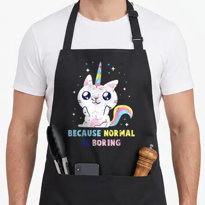Tablier de cuisine noir avec un chat blanc licorne aux yeux brillants et une queue colorée entourée d'étoiles.