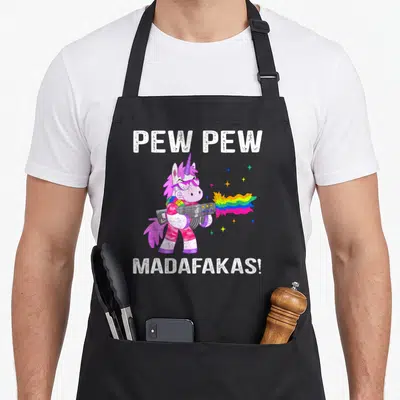 Tablier de cuisine noir avec licorne rose tirant un rayon arc-en-ciel et texte blanc distordu.