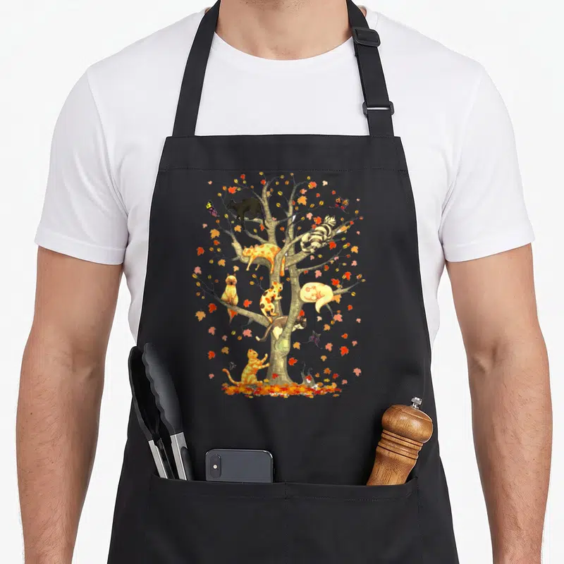 Tablier de cuisine noir avec un arbre d'automne peuplé de chats de toutes couleurs et de papillons.